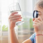 the child examines the water with magnifying glass in glass
