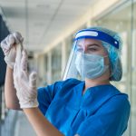 young pretty nurse in uniform wearing face shield mask protection from new infectious virus coronavirus covid 19 in clinic