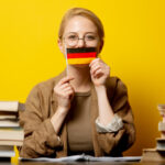 style blonde woman sitting at table with books and flag of germany on yellow